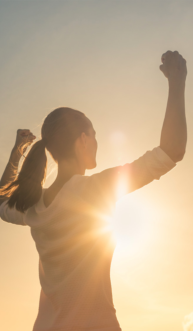 Strong confident woman flexing arms facing the sunset.