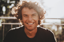 Outdoor closeup portrait of handsome freckled smiling male with curly hair, posing for social advertisement, in the city street on sunset sunlight