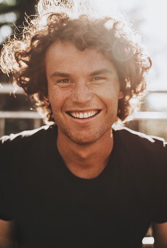 Outdoor closeup portrait of handsome freckled smiling male with curly hair, posing for social advertisement, in the city street on sunset sunlight